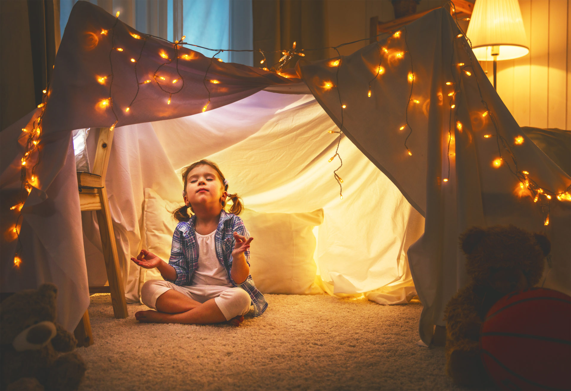 child girl playing meditates in yoga pose in tent at home before going to bed
