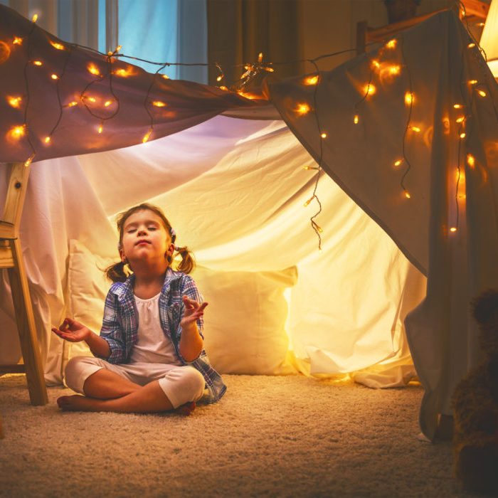 child girl playing meditates in yoga pose in tent at home before going to bed